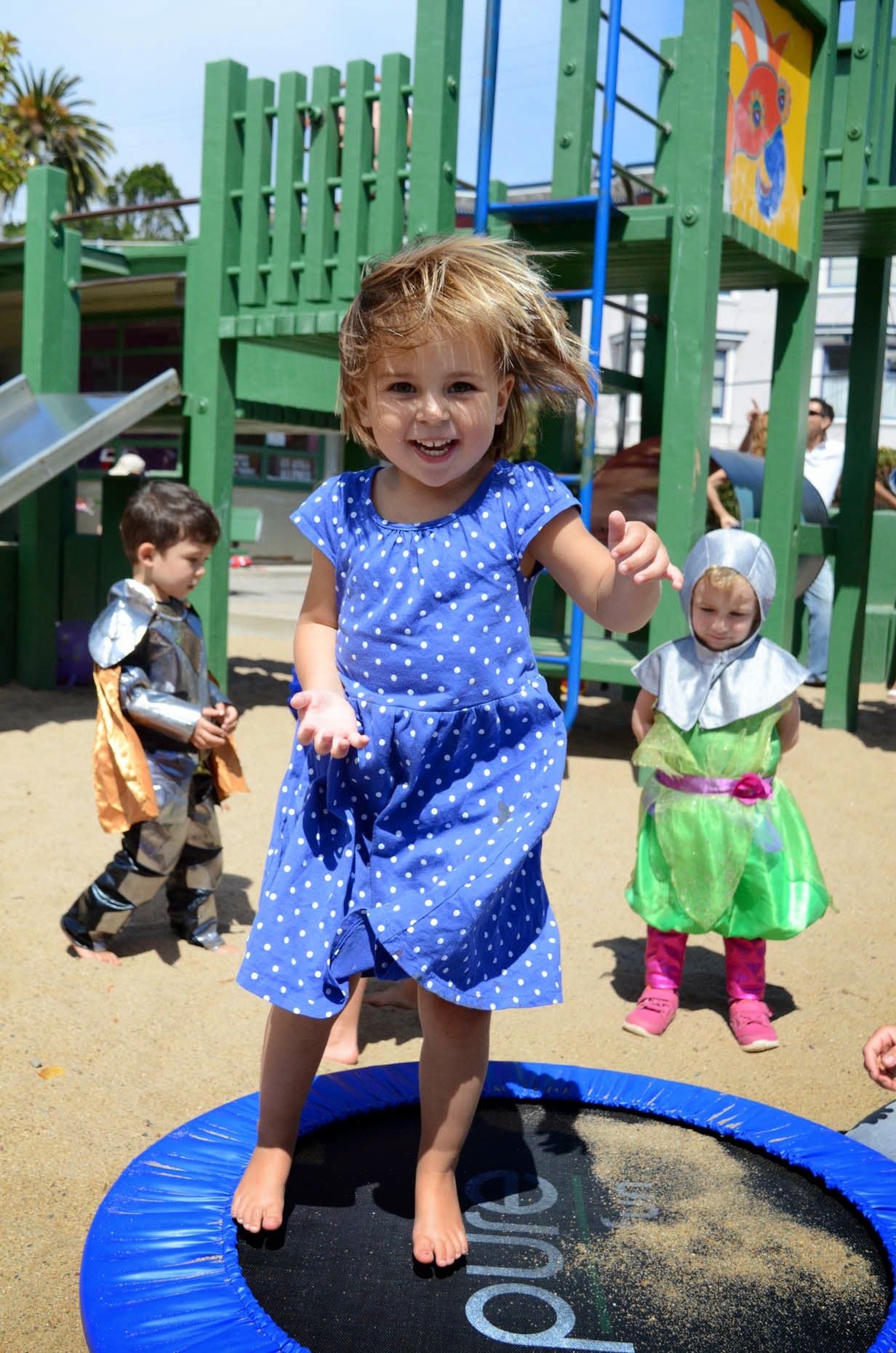 Three children in costume playing on the sand at the playground