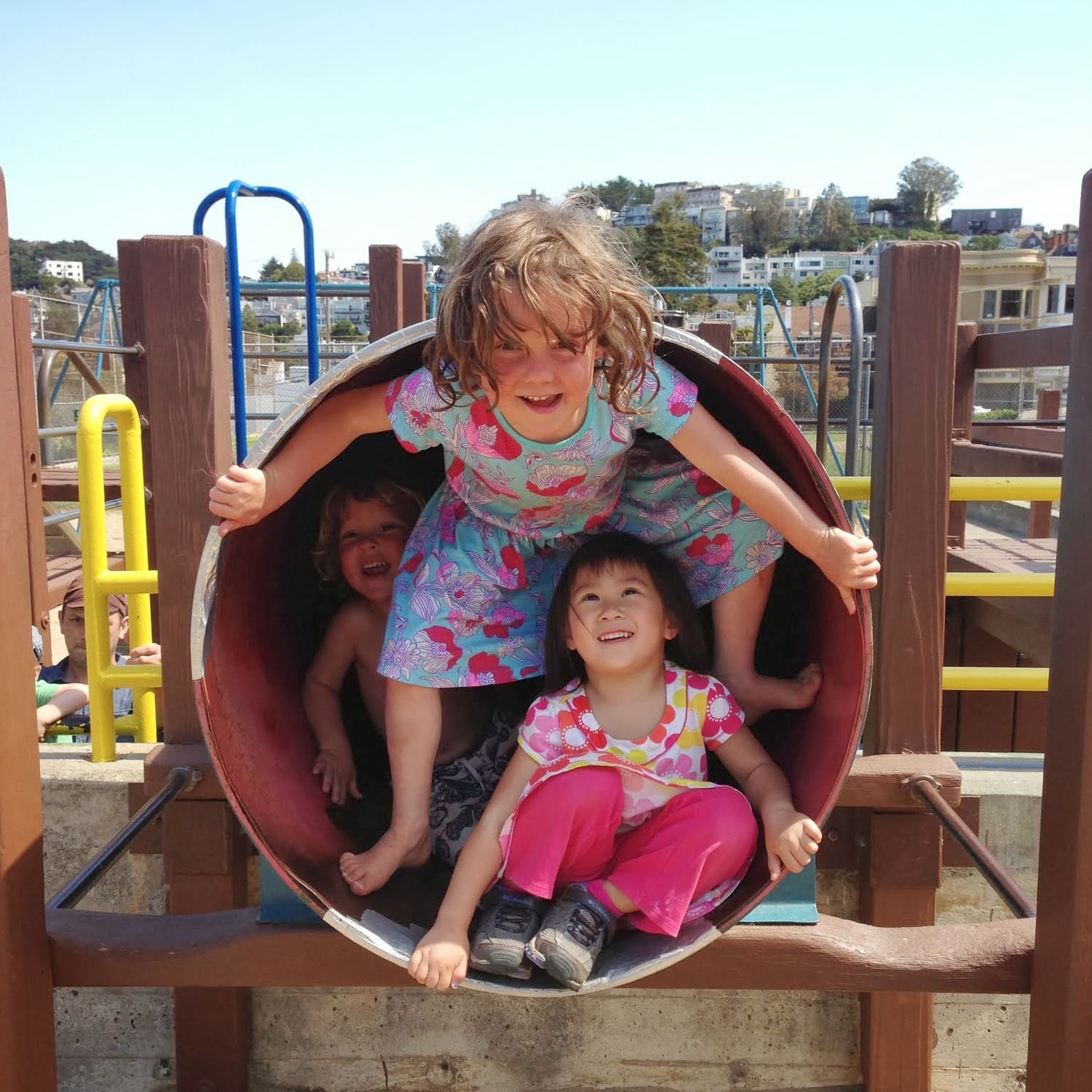 Three children laughing together inside the tunnel of the play structure